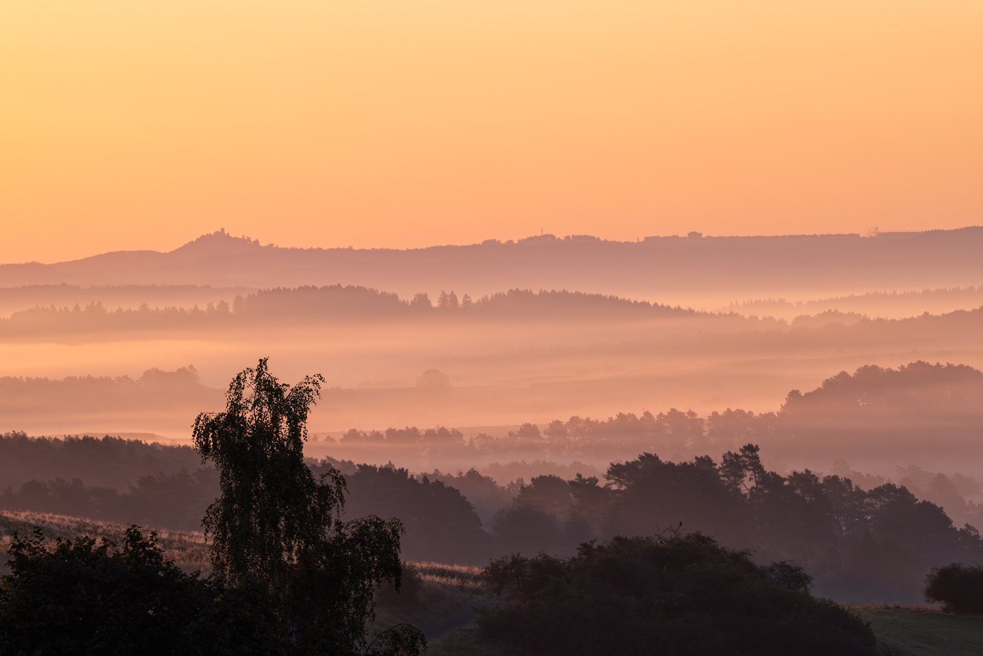 Sonnenaufgang über der Eifel. Im Hintergrund ganz oben erkennt man die Gebäude der Rennstrecke Nürburgring inkl. seiner Achterbahn und links der Nürburg.